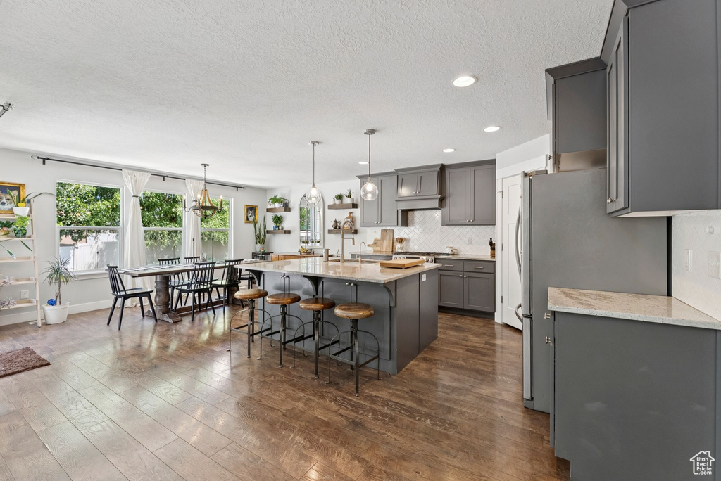Kitchen featuring gray cabinets, a breakfast bar area, a center island with sink, a textured ceiling, and decorative backsplash