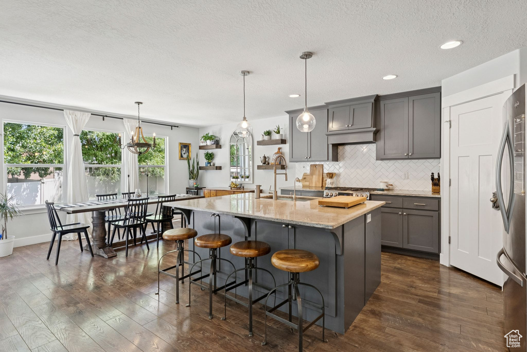 Kitchen with gray cabinetry, a kitchen island with sink, freestanding refrigerator, tasteful backsplash, and dark wood-type flooring