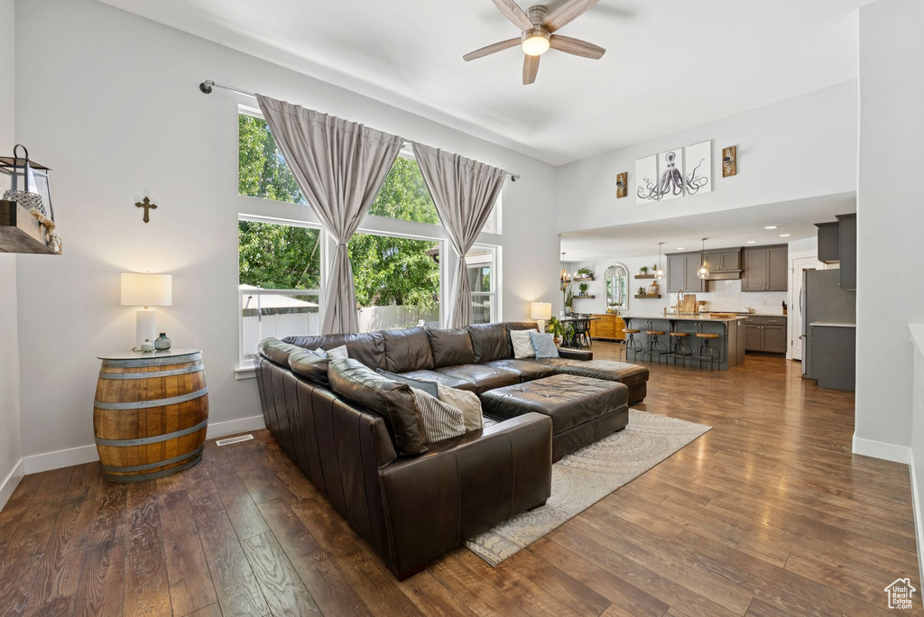 Living area with ceiling fan, dark wood-style flooring, and a towering ceiling