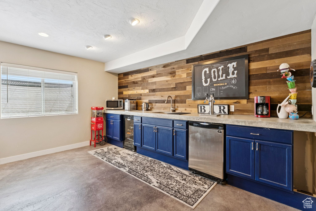 Indoor wet bar with wooden walls, stainless steel appliances, wine cooler, and concrete flooring