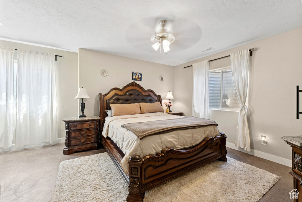 Carpeted bedroom featuring multiple windows and ceiling fan