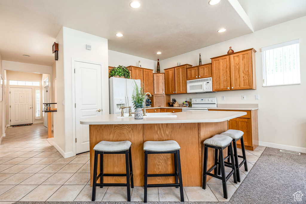 Kitchen featuring white appliances, light countertops, light tile patterned floors, a kitchen breakfast bar, and a kitchen island with sink
