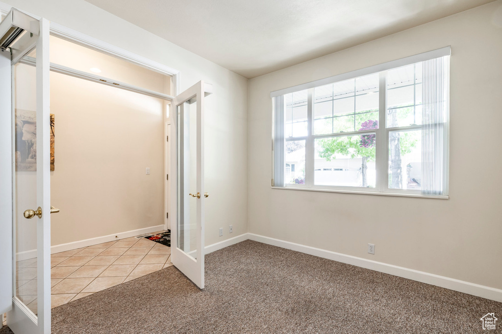 Unfurnished bedroom with french doors, light carpet, a wall mounted air conditioner, and light tile patterned flooring