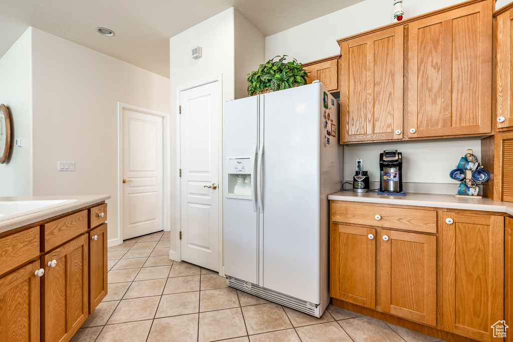 Kitchen with white refrigerator with ice dispenser, light tile patterned floors, light countertops, and brown cabinetry