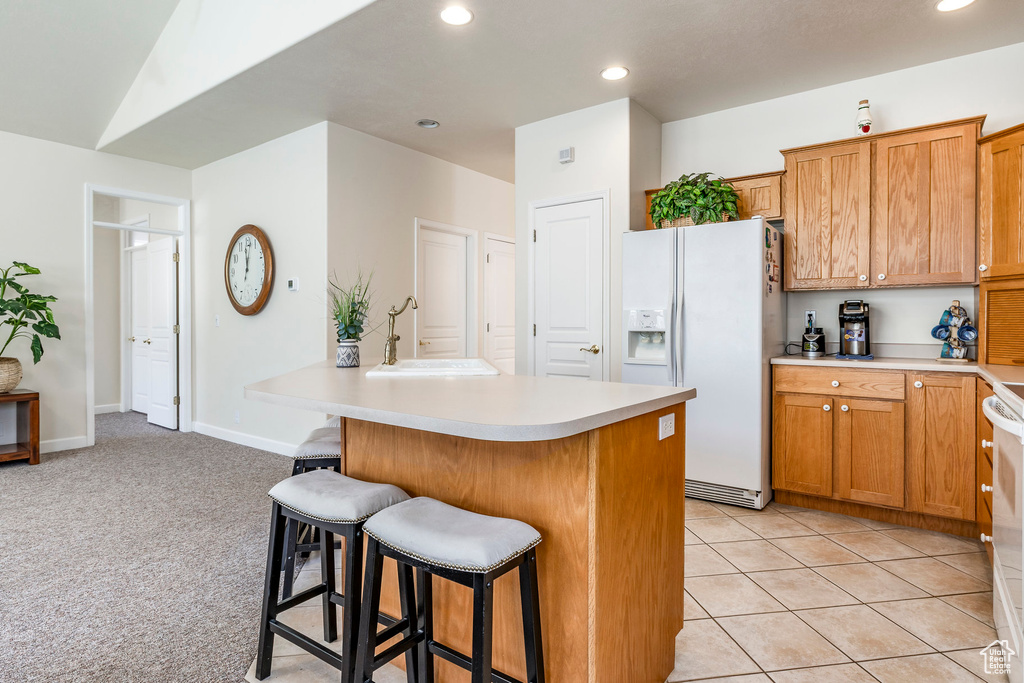 Kitchen with white fridge with ice dispenser, a kitchen breakfast bar, light countertops, recessed lighting, and brown cabinetry