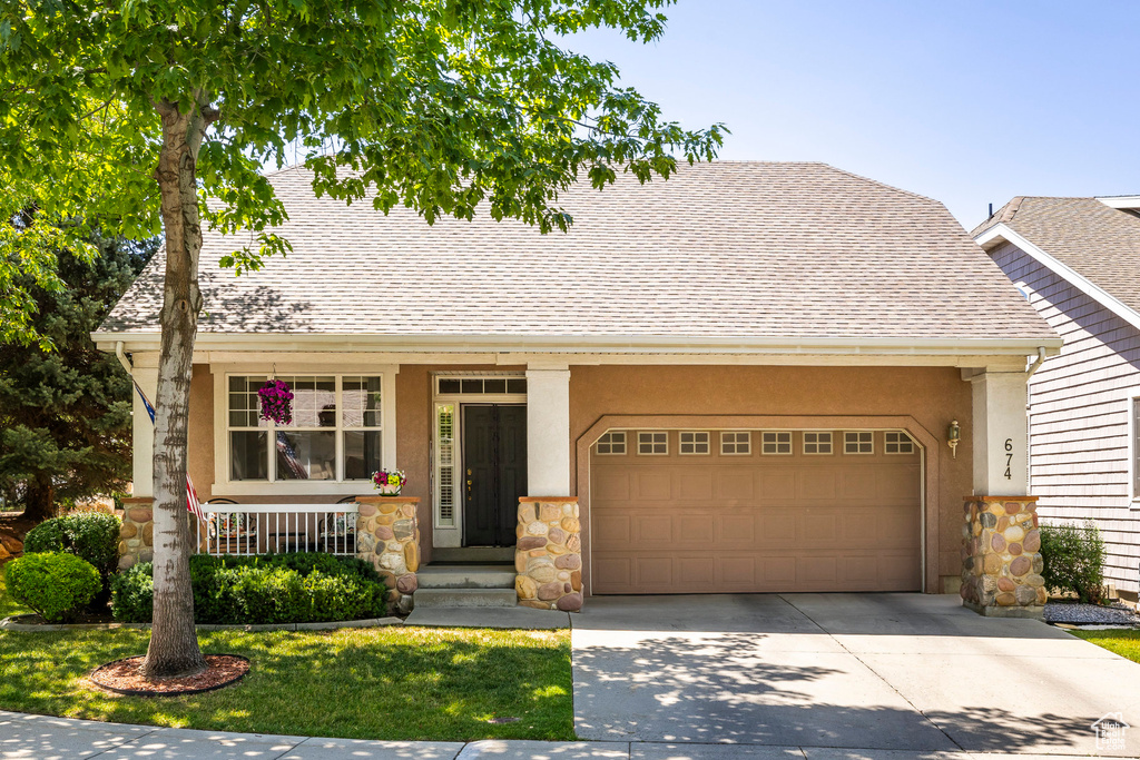 View of front of home with driveway, roof with shingles, stucco siding, and stone siding