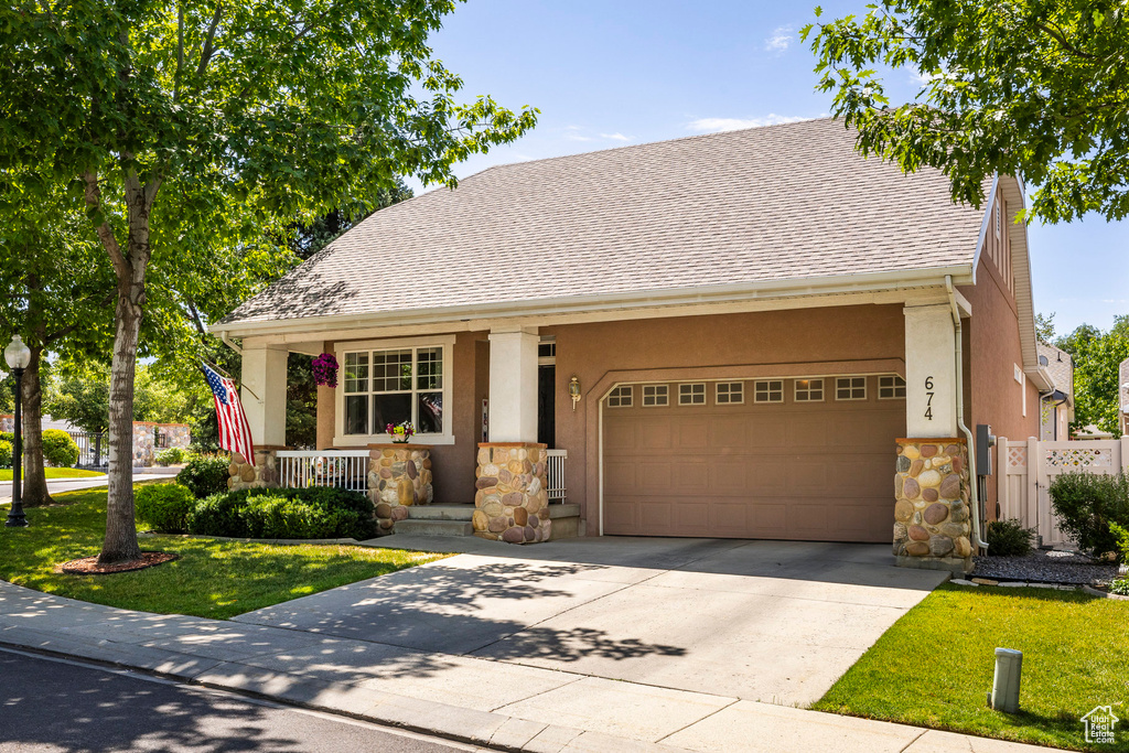 View of front of house with stone siding, stucco siding, a porch, a garage, and concrete driveway