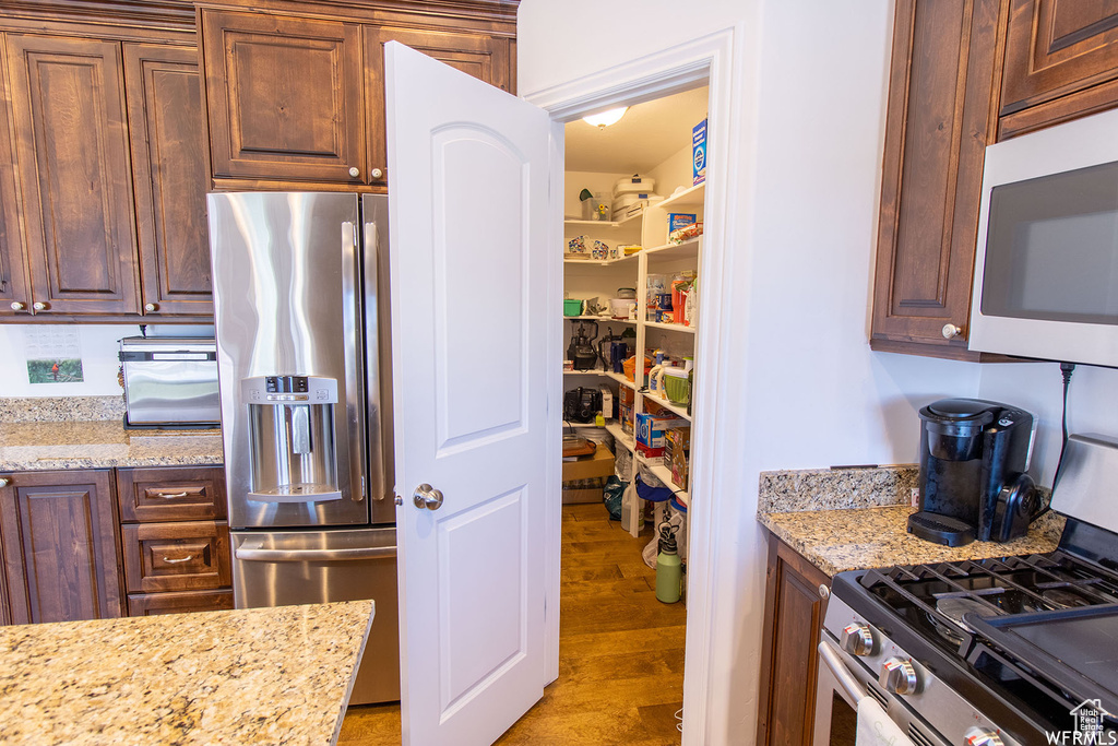Kitchen with appliances with stainless steel finishes, light wood-style flooring, and light stone counters