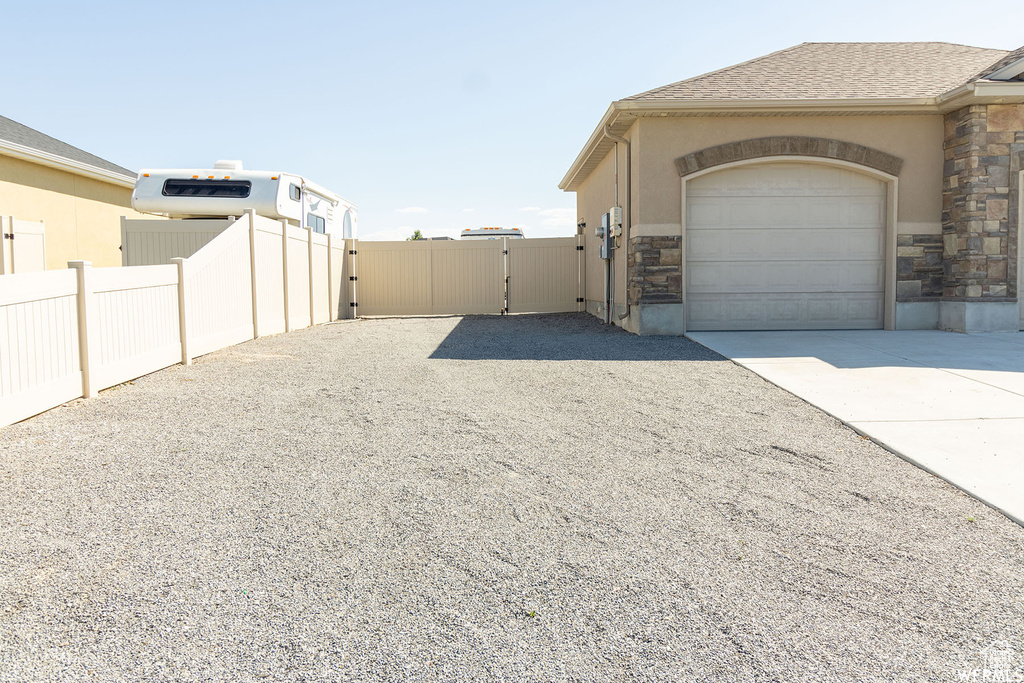 View of side of home featuring driveway, a gate, stone siding, an attached garage, and stucco siding