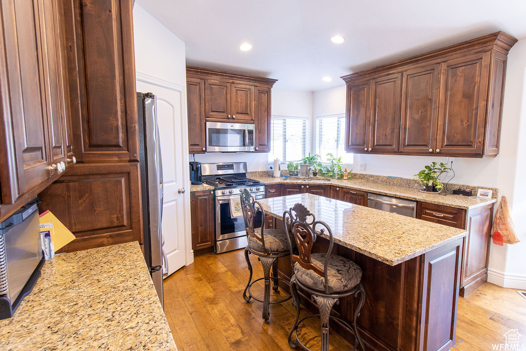 Kitchen with appliances with stainless steel finishes, light wood finished floors, light stone counters, recessed lighting, and a center island