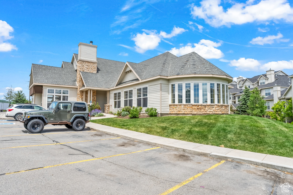View of front of home featuring stone siding, uncovered parking, a chimney, and a front lawn