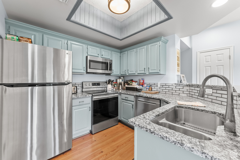 Kitchen featuring appliances with stainless steel finishes, light wood-type flooring, light stone counters, and blue cabinets