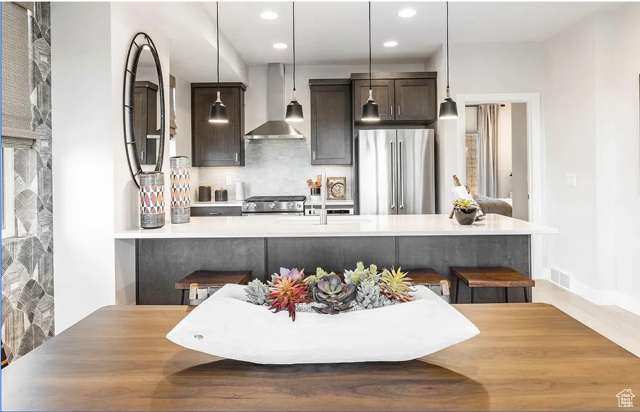 Kitchen featuring wall chimney range hood, stainless steel appliances, decorative backsplash, dark brown cabinets, and light countertops
