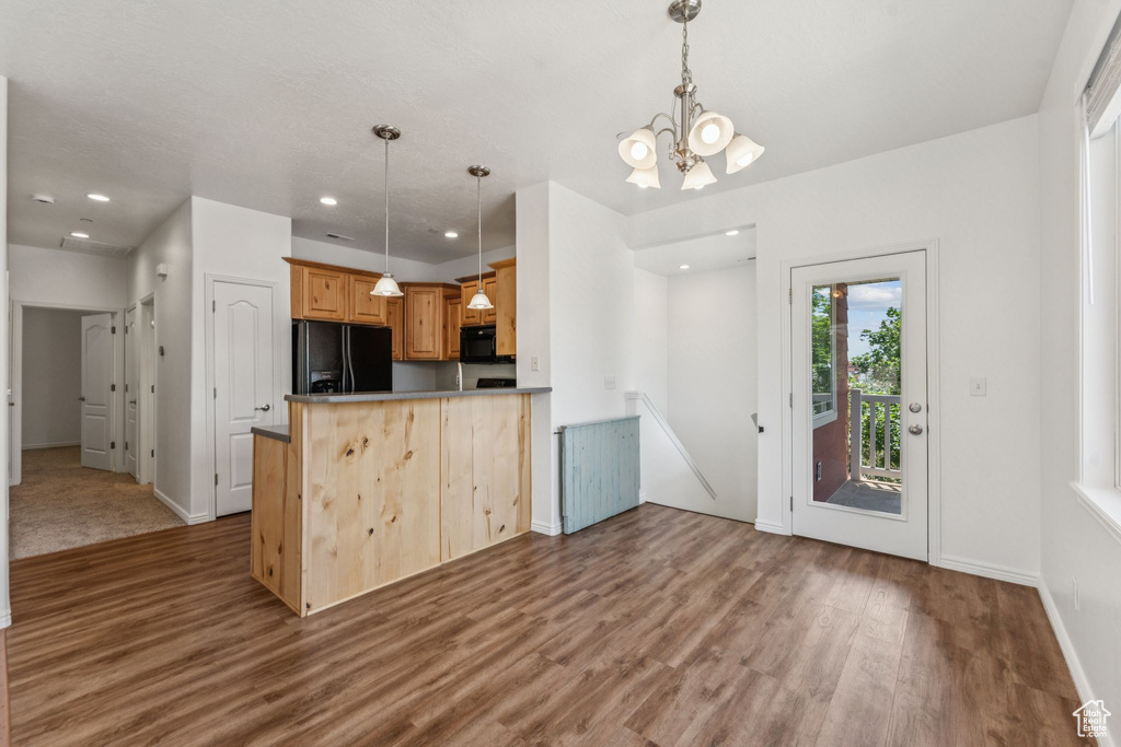 Kitchen with black appliances, wood finished floors, a chandelier, pendant lighting, and a peninsula
