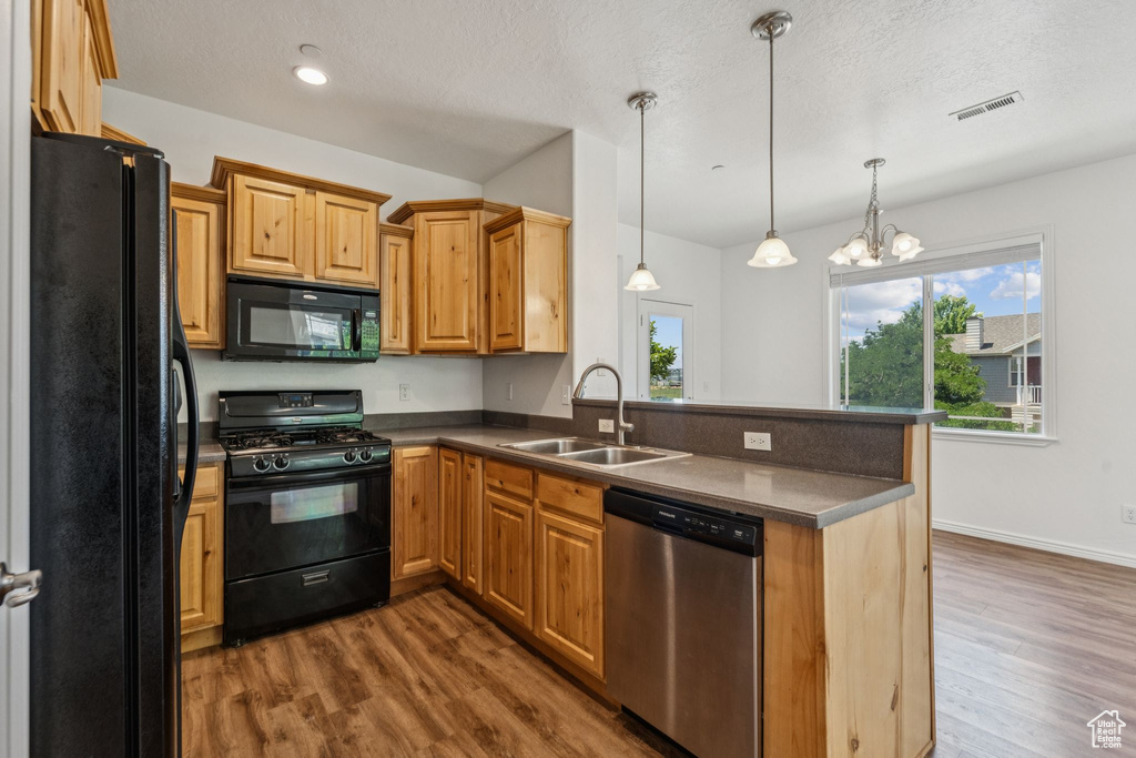 Kitchen featuring black appliances, dark countertops, a peninsula, dark wood-style floors, and decorative light fixtures