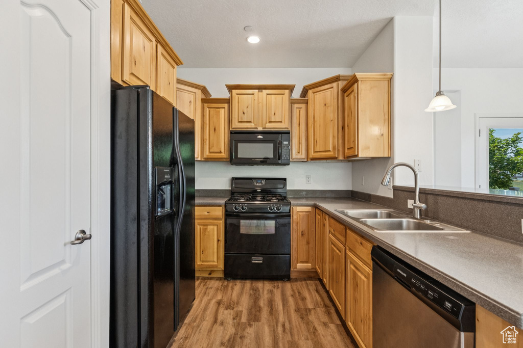 Kitchen featuring black appliances, light wood-style flooring, pendant lighting, and dark countertops
