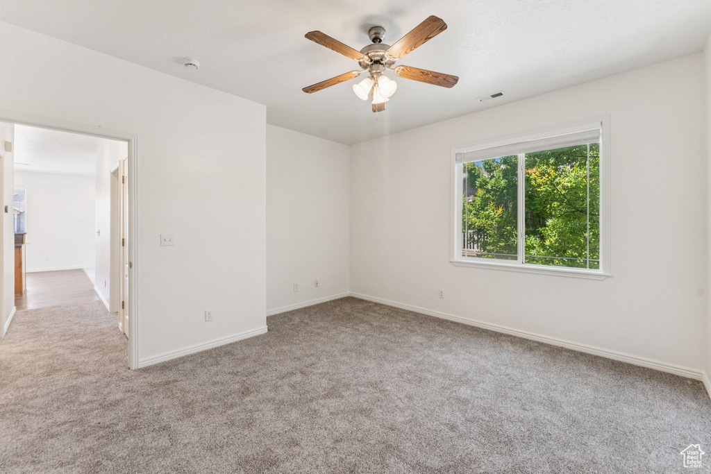 Carpeted spare room featuring a ceiling fan and baseboards