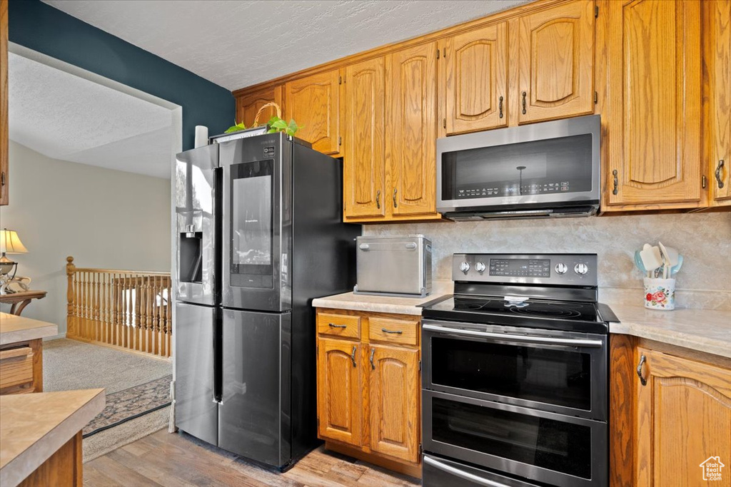 Kitchen with appliances with stainless steel finishes, light countertops, decorative backsplash, light wood-style flooring, and brown cabinetry
