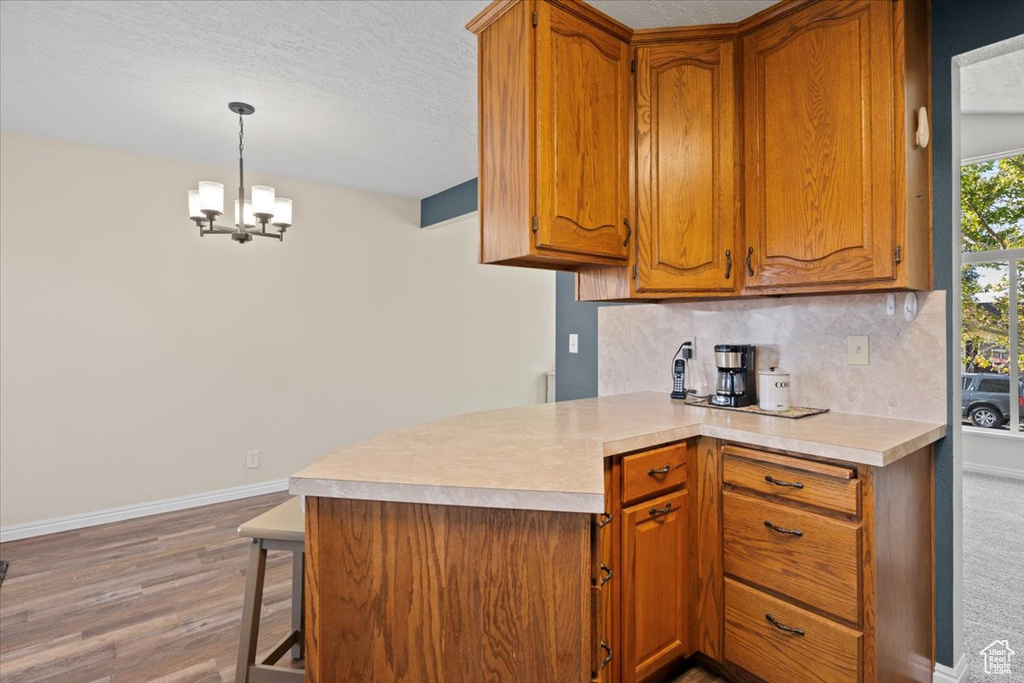 Kitchen featuring brown cabinets, light wood-type flooring, light countertops, a chandelier, and decorative backsplash
