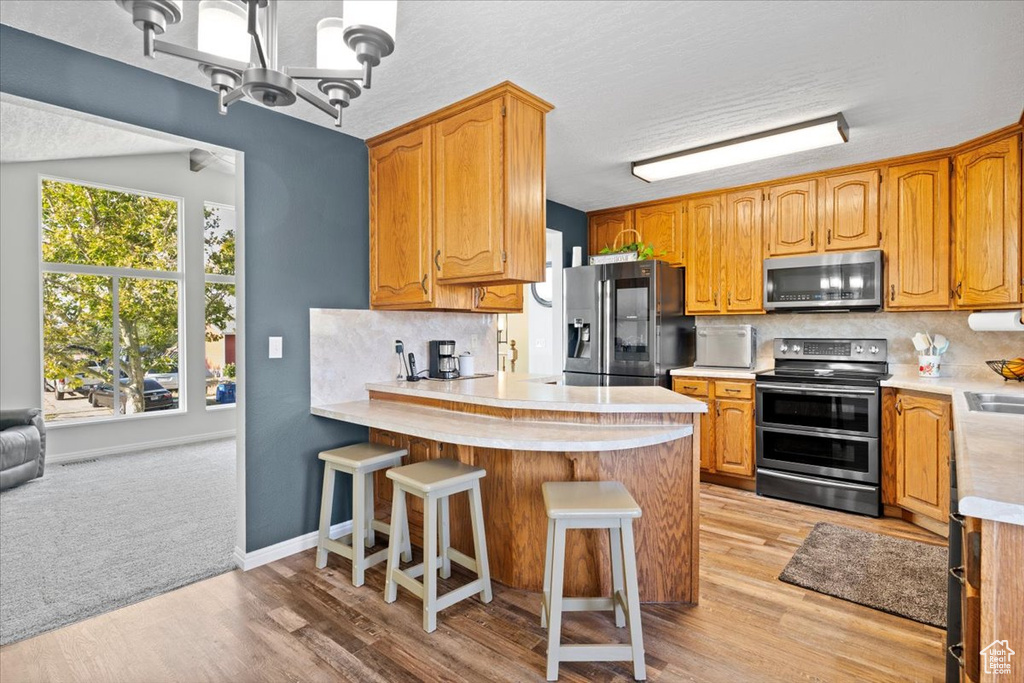 Kitchen with appliances with stainless steel finishes, a peninsula, light countertops, and backsplash
