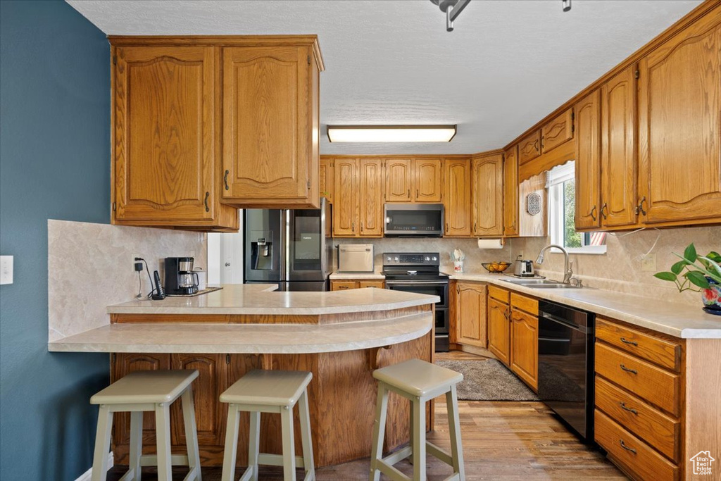 Kitchen with stainless steel appliances, a peninsula, light countertops, tasteful backsplash, and light wood-style flooring
