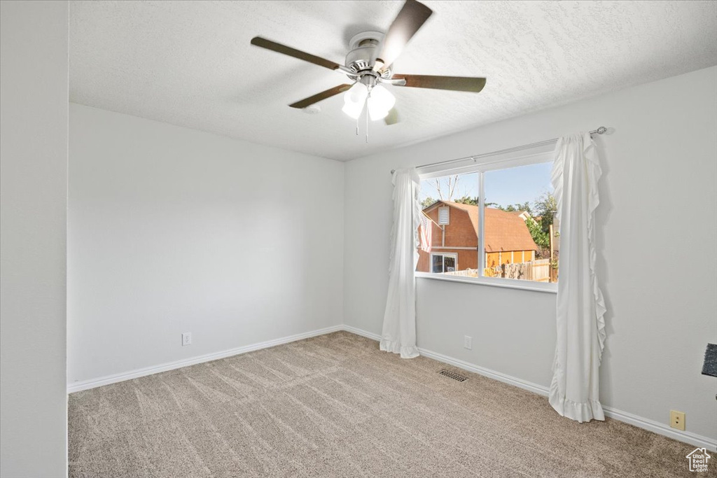 Empty room featuring a ceiling fan, carpet, and a textured ceiling