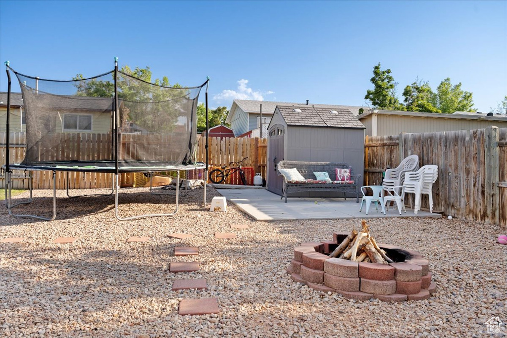 Fenced backyard with a trampoline, a storage shed, a fire pit, and a patio area