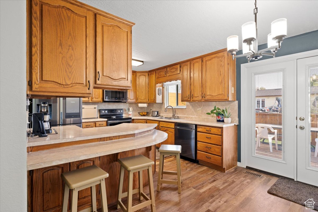 Kitchen with stainless steel appliances, a peninsula, light countertops, light wood finished floors, and tasteful backsplash