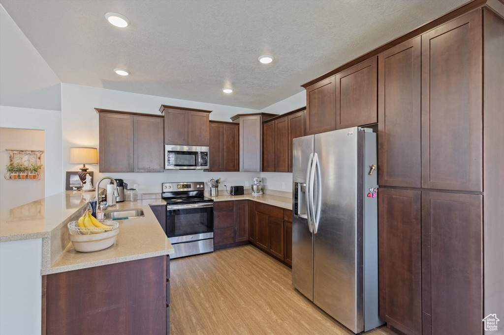 Kitchen with appliances with stainless steel finishes, a peninsula, light wood-style flooring, recessed lighting, and dark brown cabinets
