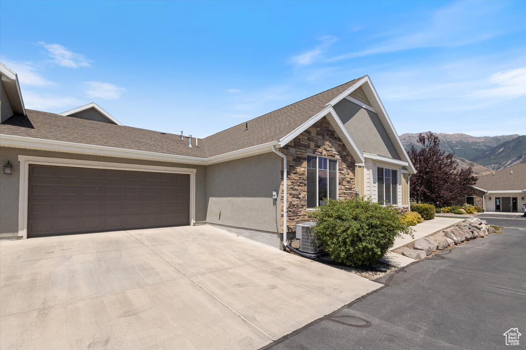 Ranch-style house featuring stucco siding, stone siding, concrete driveway, a garage, and a mountain view