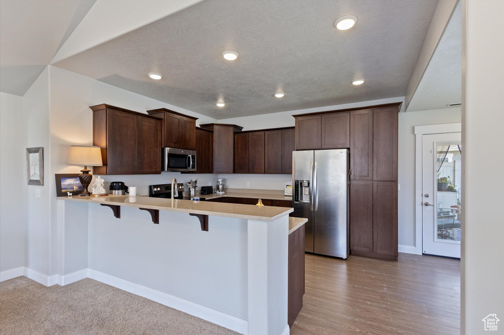 Kitchen featuring stainless steel appliances, a peninsula, a kitchen bar, dark brown cabinets, and light countertops