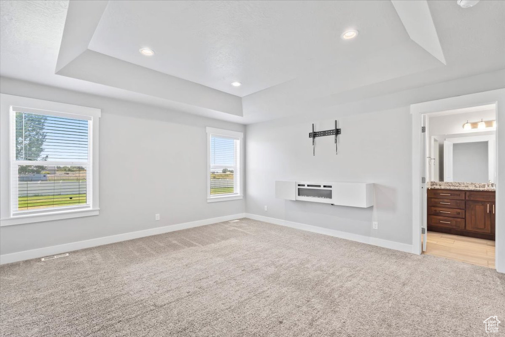 Unfurnished living room featuring a tray ceiling, light carpet, and recessed lighting