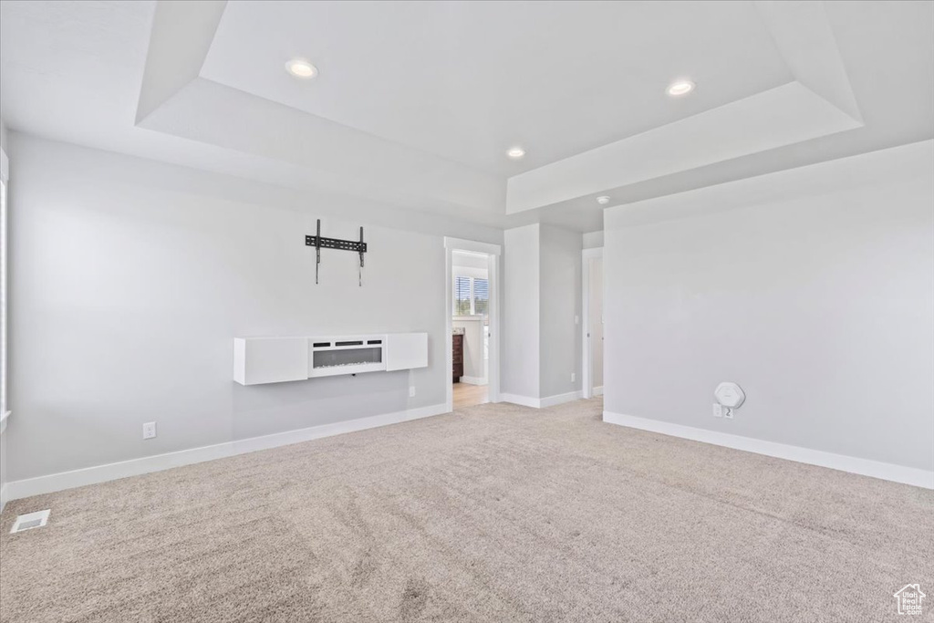 Unfurnished living room featuring a raised ceiling, recessed lighting, and light colored carpet