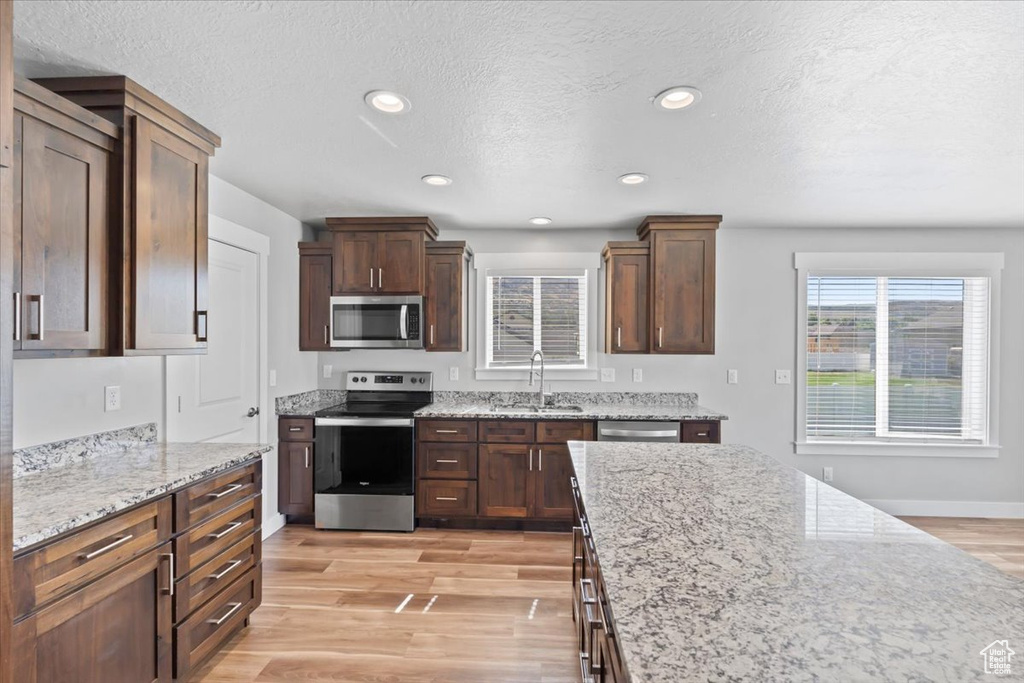 Kitchen with stainless steel appliances, light wood-type flooring, light stone countertops, a textured ceiling, and recessed lighting