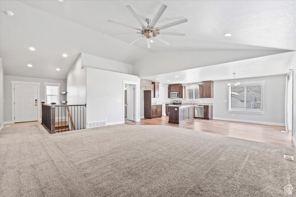 Unfurnished living room with light carpet, ceiling fan, lofted ceiling, a chandelier, and recessed lighting
