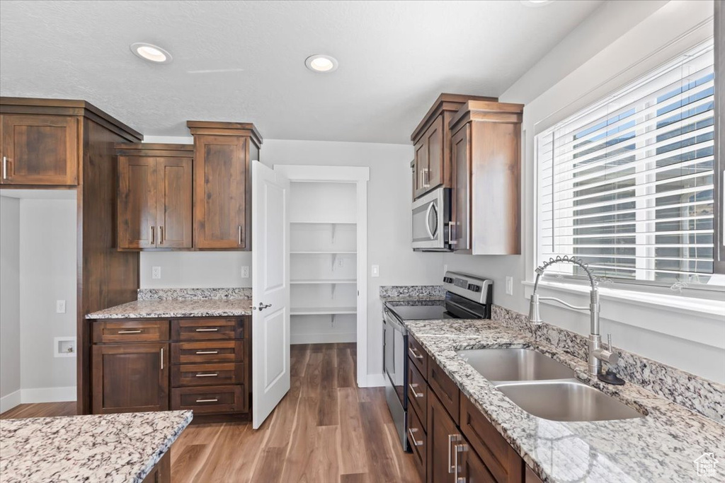 Kitchen featuring stainless steel appliances, wood finished floors, light stone countertops, and recessed lighting