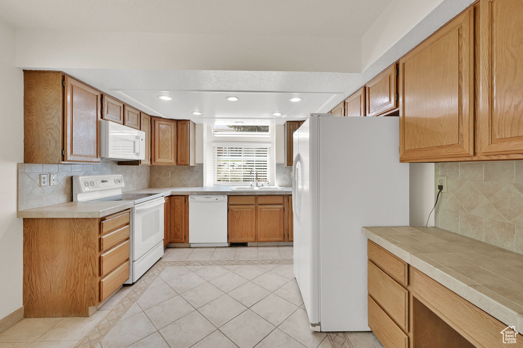 Kitchen featuring white appliances, backsplash, recessed lighting, light tile patterned flooring, and brown cabinetry