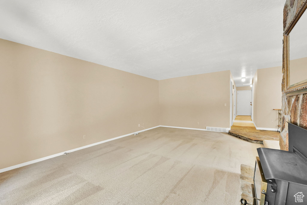 Unfurnished living room featuring a fireplace, carpet floors, and a textured ceiling