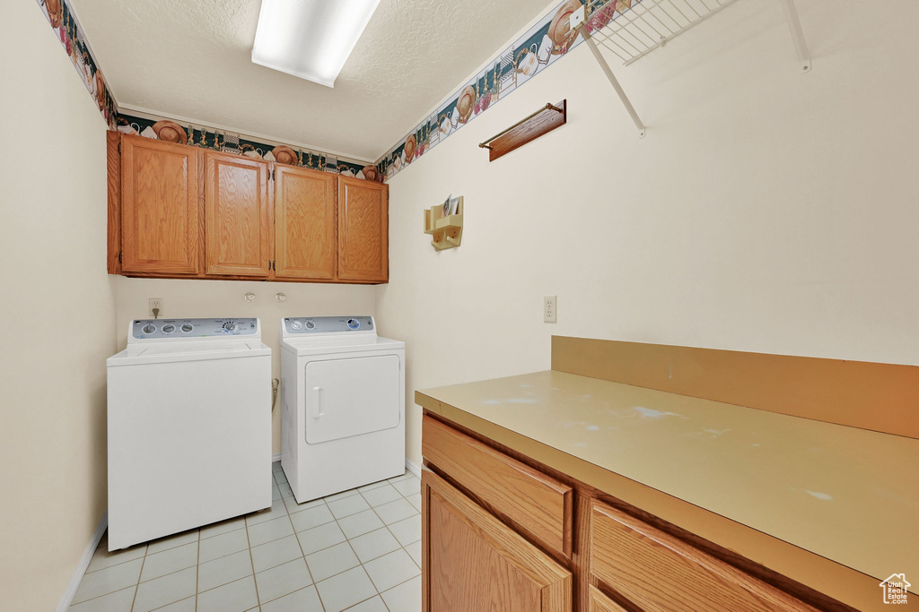 Washroom featuring cabinet space, washing machine and clothes dryer, and light tile patterned flooring
