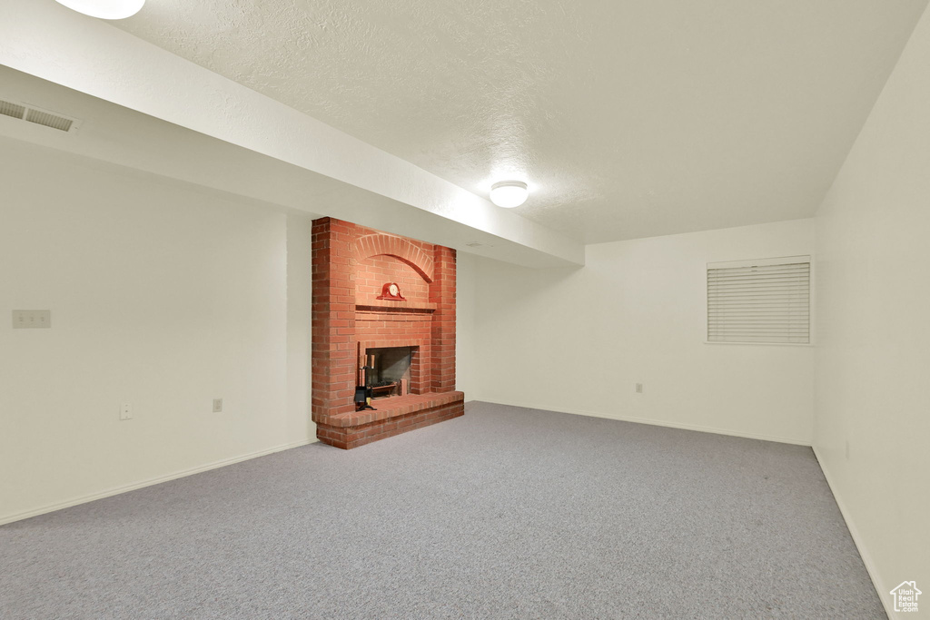 Finished below grade area with a brick fireplace, a textured ceiling, and carpet flooring