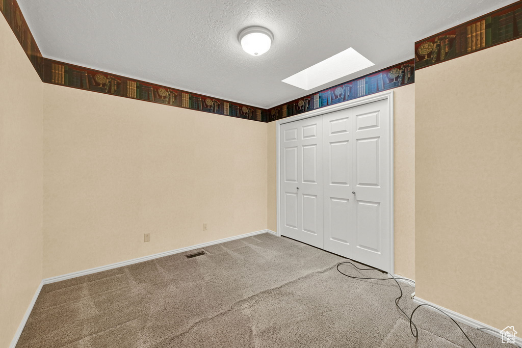 Unfurnished bedroom featuring a skylight, carpet flooring, a textured ceiling, and a closet