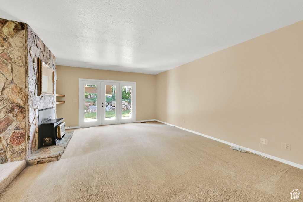Unfurnished living room featuring a wood stove, carpet flooring, french doors, and a textured ceiling