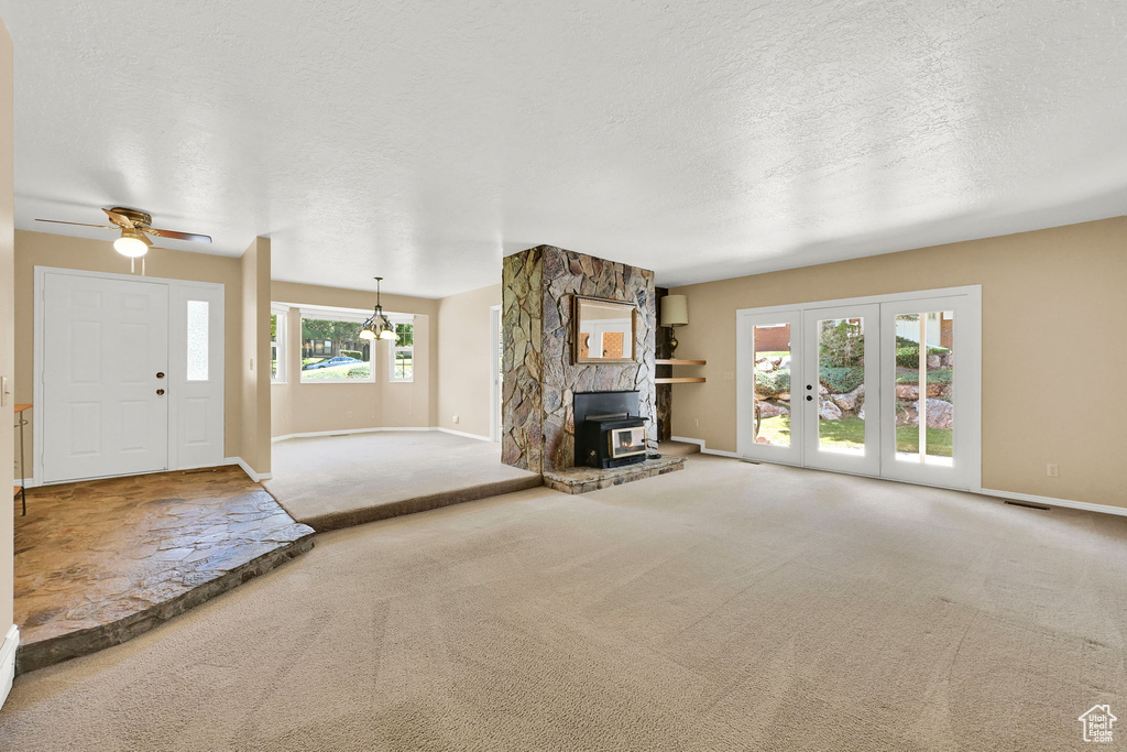 Unfurnished living room with carpet, a textured ceiling, french doors, a wood stove, and ceiling fan