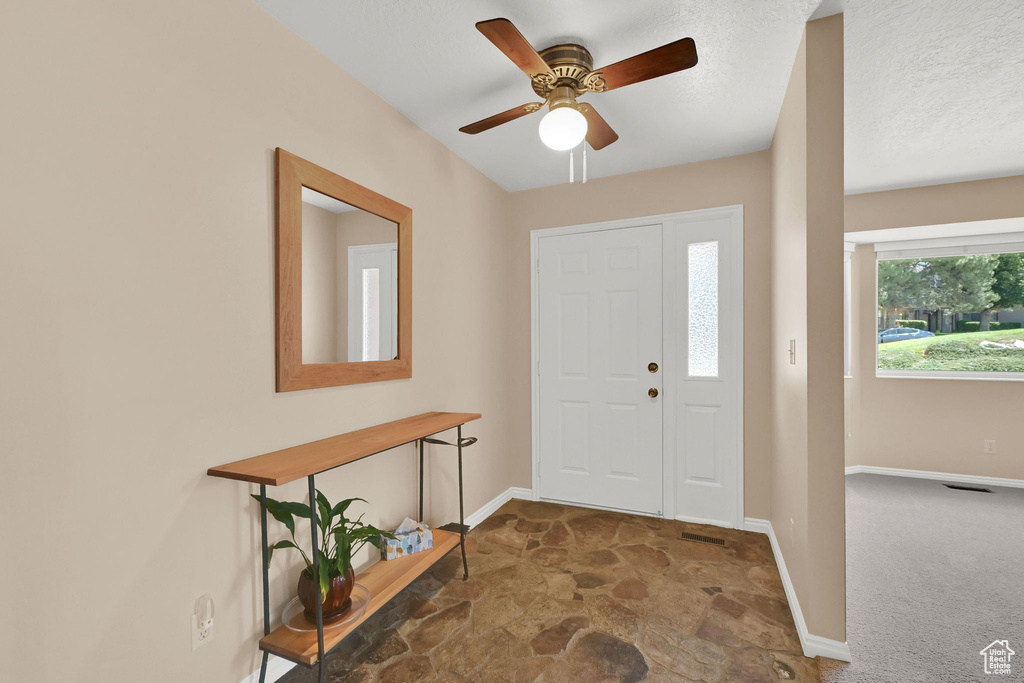 Foyer entrance with stone finish flooring, ceiling fan, and carpet flooring