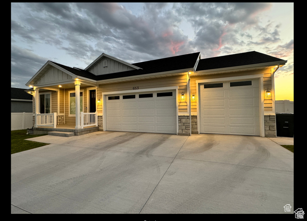Craftsman-style home featuring a porch, board and batten siding, an attached garage, driveway, and stone siding