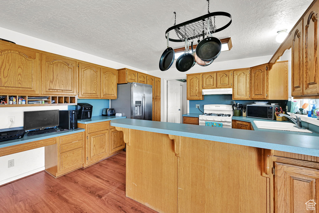 Kitchen with appliances with stainless steel finishes, under cabinet range hood, a textured ceiling, light wood-style flooring, and a peninsula