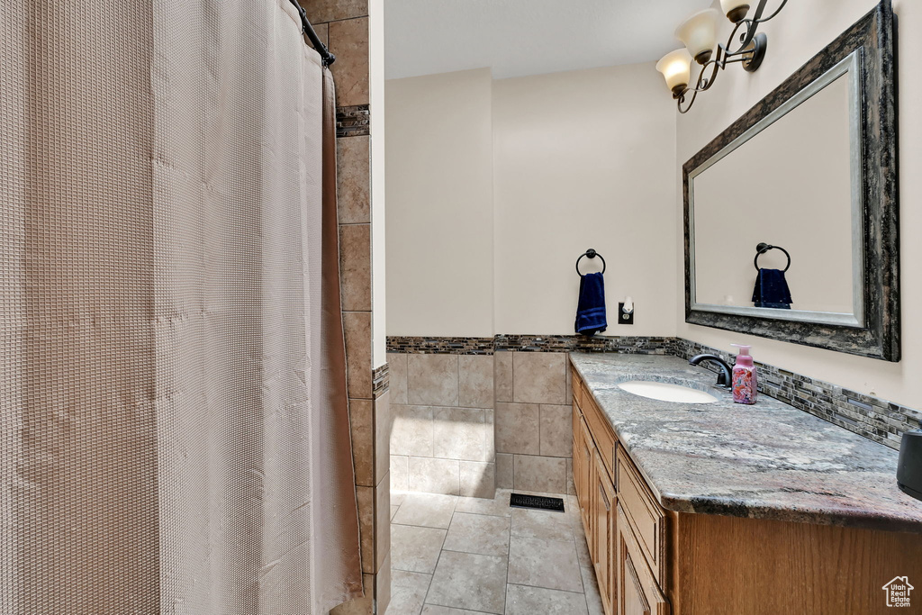 Full bathroom with vanity, tile walls, a shower with shower curtain, wainscoting, and tile patterned floors