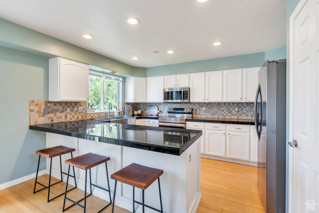 Kitchen featuring stainless steel appliances, a peninsula, light wood finished floors, a breakfast bar area, and white cabinetry