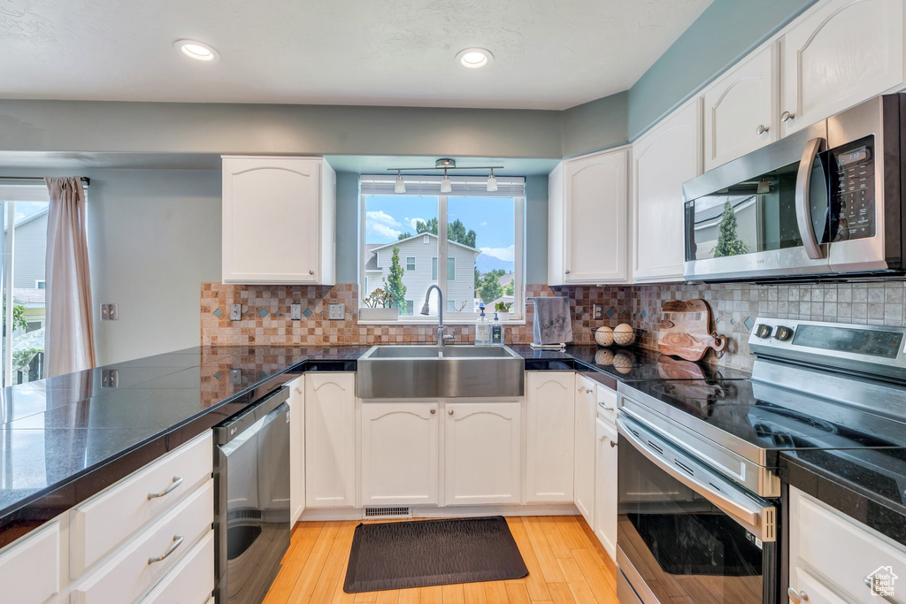 Kitchen featuring stainless steel appliances, white cabinets, light wood-style floors, a peninsula, and recessed lighting