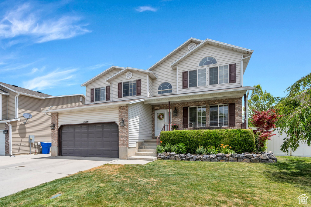 View of front of home featuring driveway, a front yard, brick siding, and covered porch